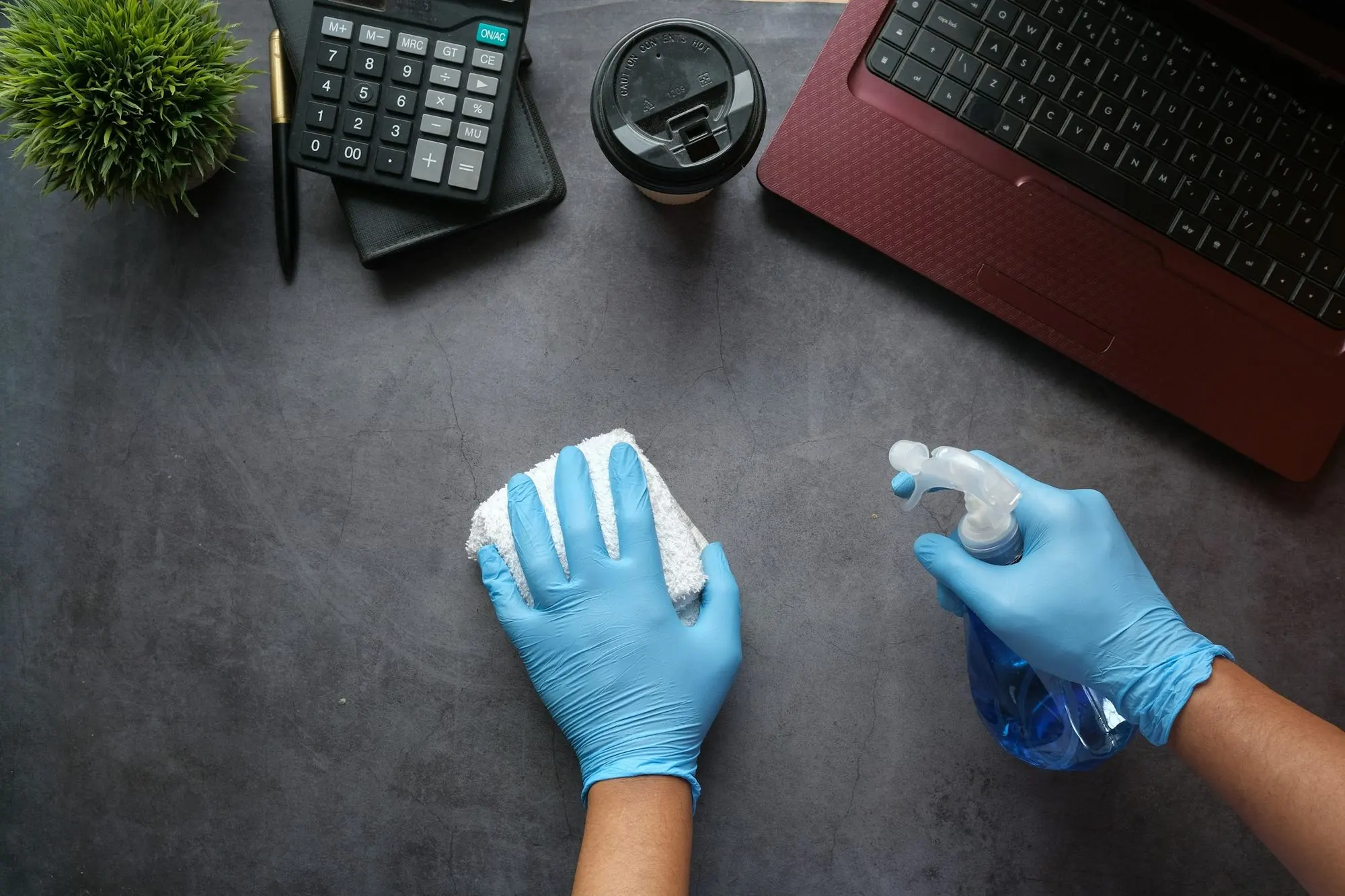 Hände in blauen Handschuhen reinigen eine Schreibtischoberfläche